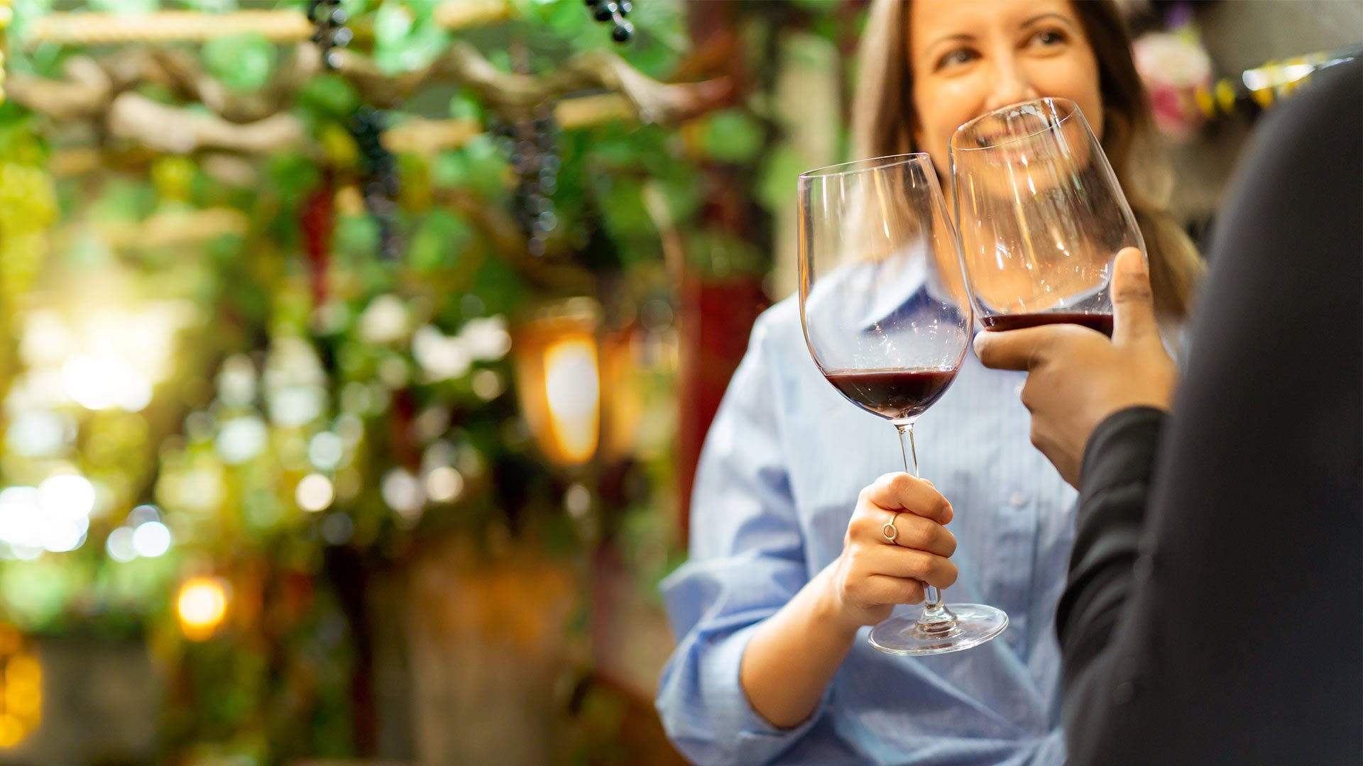 Two people toasting with glasses of red wine beneath grapevines at a winery
